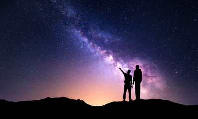 Milky Way with silhouette of a family. Father and a son who pointing finger in night starry sky on...
