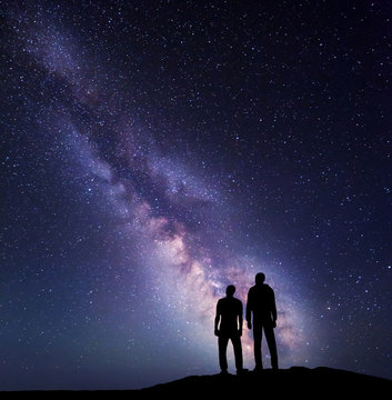 Silhouette of a family on the mountain. Father and a son  on the background of Milky Way. Night landscape. Beautiful Universe. Space. Travel background with sky full of stars