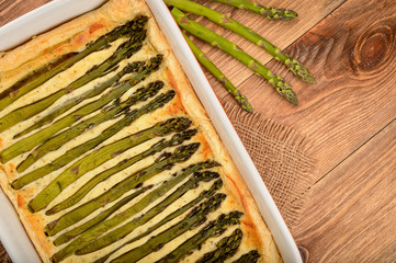 Tart with green asparagus on wooden table.