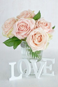 Pink roses flowers in a vase and letters "love" Floral gift for a wedding or birthday.