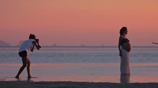 Photoshooting of pregnant woman at the beach at sunset