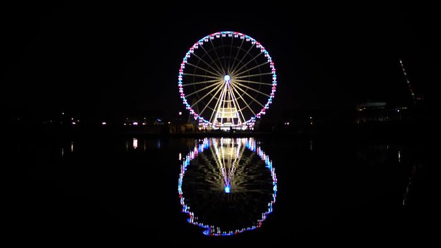 Night cityscape with illuminated Ferris wheel reflection on dark water surface