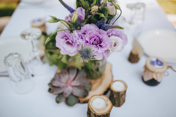 decoration of flowers, herbs and wooden elements on a festive table with a white cloth, which stands on a green lawn in the forest