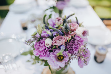 decoration of flowers, herbs and wooden elements on a festive table with a white cloth, which stands on a green lawn in the forest