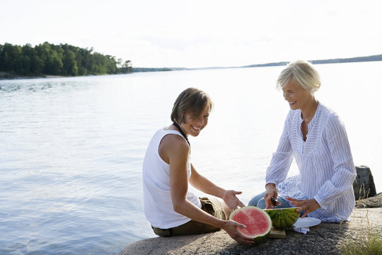 Two women eating watermelon by the sea, Sweden.