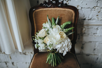 bridal bouquet of white flowers and greenery is on a vintage chair against a white brick wall in loft