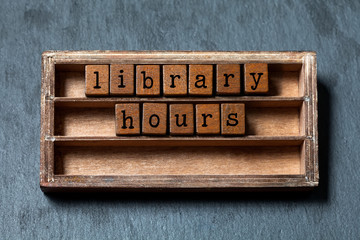 Library hours conept. Vintage blocks with letters, aged wooden box. Gray stone background, macro
