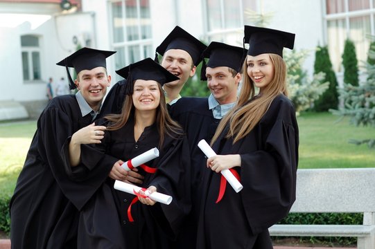 Group of laughing university graduates with diplomas in their hands