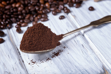 Ground coffee in spoon with coffee beans.