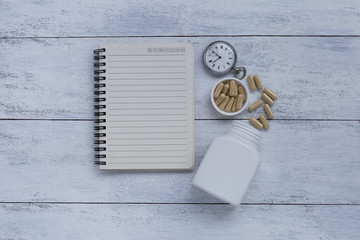 Herb capsule with blank notebook and watch on white wood background