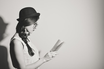 Black white picture of beautiful girl reading a book against light wall background