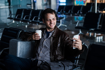 Fototapeta na wymiar Portrait of a young man laughing and taking selfie with coffee at the airport waiting his flight