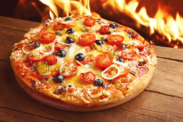 Delicious hot pizza on wooden table against fire flame background