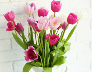 Obraz premium Beautiful tulips in vase on white brick wall background