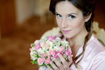 Beauty bride in dressing gown with bouquet and lace veil indoors. Beautiful model girl in colorful wedding robe. Female portrait of cute lady. Woman with hairstyle