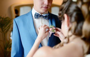 Groom and bride are wearing a boutonniere indoors. Male portrait of handsome guy. Beautiful model boy in colorful wedding clothes. Man is posing