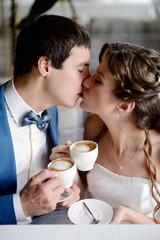 Wedding couple indoors is drinking coffee. Beautiful model girl in white dress. Man in suit. Beauty bride with groom. Female and male portrait. Woman with lace veil. Cute lady and handsome guy