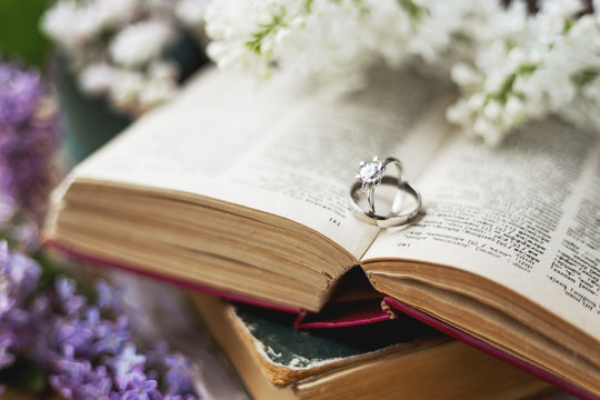 Pair of wedding rings with diamond. Rustic background with old books and lilac flowers. Retro background. Selected soft focus.
