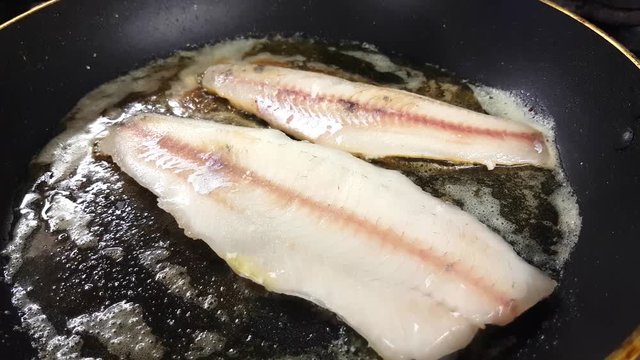 Frying fresh zander fillets, on a frying pan, inside a restaurant kitchen