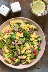 Pasta primavera with green asparagus, pea, broccoli, mushroom and tomato in cream sauce served on plate, photographed overhead on slate with natural light