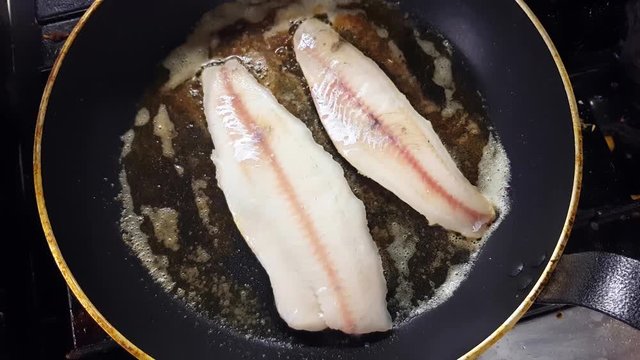 Frying white zander fillets, on a frying pan, inside a restaurant kitchen