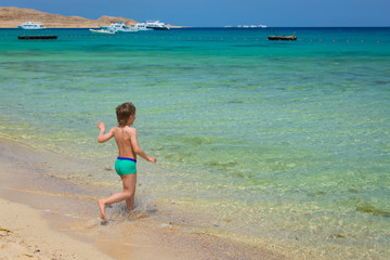 Fototapeta na wymiar boy runs into the blue sea of the beautiful, white beach blue sky