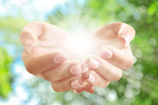 Light in hands on green nature background. Concept of taking care, protection, helping and assistance