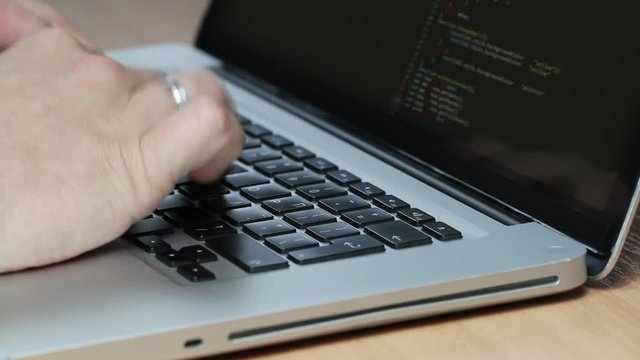 Closeup shot of a macbook laptop keyboard while a programmer types code into two editor windows, all logos covered