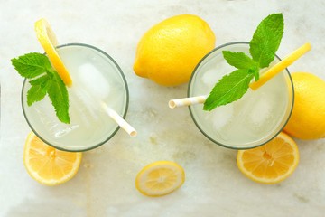 Two glasses of lemonade with mint, overhead view on a white marble background