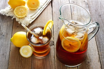 Pitcher of fresh lemon iced tea with filled glass on a rustic wooden background