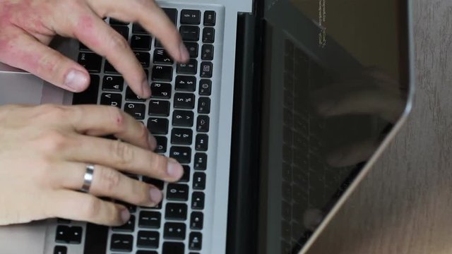 Programming on a macbook laptop, slightly sped up so that more code is visible. Screen shows both computer code and reflection of programmers hands