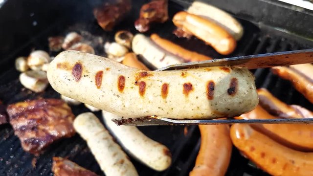 Picking up a grilled bratwurst, from a barbeque full of sausages, champignons and ribs
