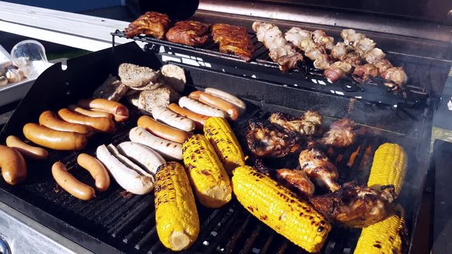 Opening a gas barbeque, full with sausages, pork loin, ribs, champignons, chicken and corn