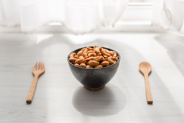 Salty cashew nuts in black ceramic bowl on wood table with windo