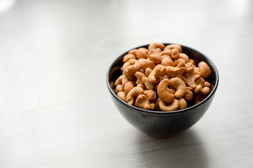 Salty cashew nuts in black ceramic bowl on gray wood table