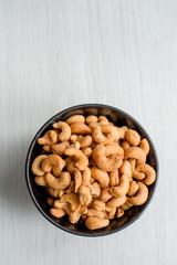 Salty cashew nuts in black ceramic bowl on gray wood table