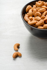 Salty cashew nuts in black ceramic bowl on gray wood table