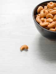 Salty cashew nuts in black ceramic bowl on gray wood table