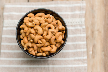 salty cashew nuts in black ceramic bowl on wood table