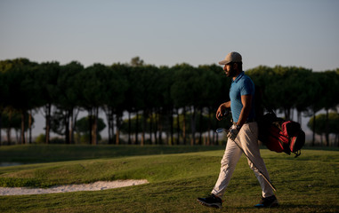 Obraz premium golfer walking and carrying golf bag at beautiful sunset