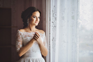 Fototapeta premium Portrait of beautiful young brunette woman bride with hand near face in white Wedding Dress.