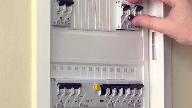 Hand checking and turning on circuit breakers in electrical fuse box at his house
