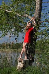 Beautiful dancer in red dress standing at a tree and sunbathing