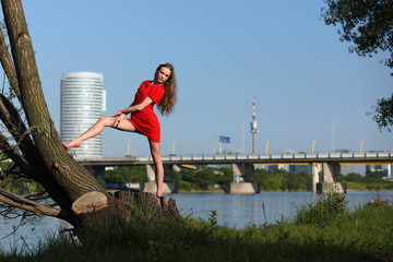 Beautiful ballerina in red dress dancing barefoot at a river in the evening