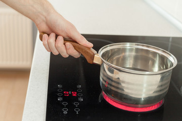 Hand holding a saucepan in modern kitchen with induction stove