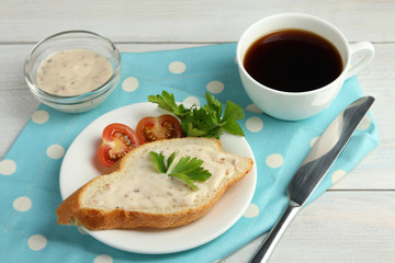 the sauce slathered on a baguette with tomatoes and herbs near to the coffee Cup on a napkin on wooden background