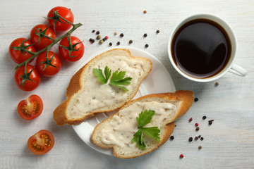 the sauce slathered on a baguette with tomatoes and herbs near to the coffee Cup  on wooden background