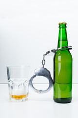 Concept image of drinking illegally featuring a beer bottle and a pair of handcuffs