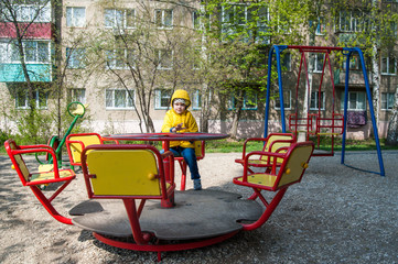 The girl in the yellow jacket sitting on the carousel at the pla