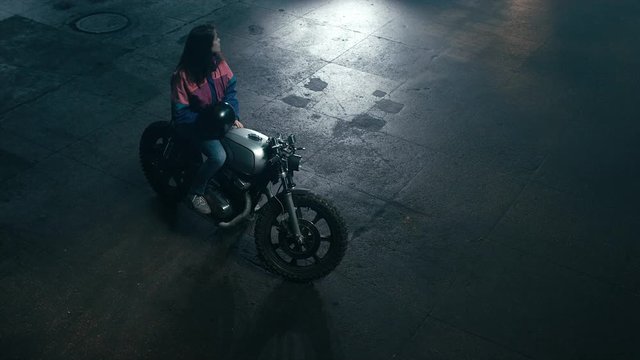 Wide overhead shot of young Caucasian female biker sitting on a motorcycle at night. 60 FPS slow motion Blackmagic URSA Mini RAW graded footage